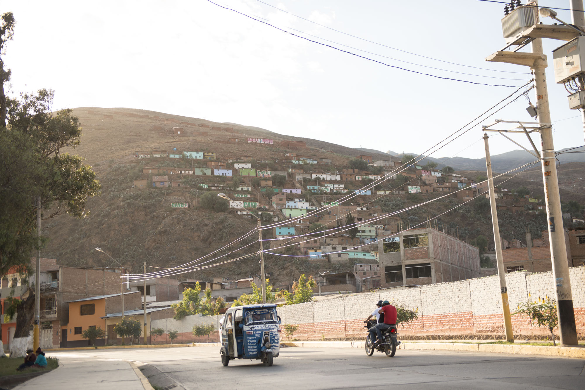 A taxi and motorcycle cruise at the base of a mountain.